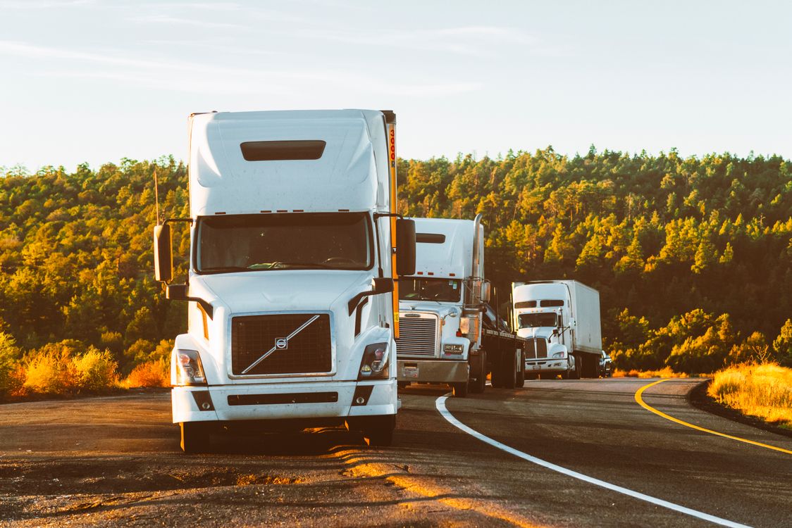 Comboio de caminhões pesados trafegando em rodovia, representando o transporte rodoviário de cargas no Brasil